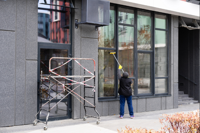 Maintenance worker cleaning the exterior windows of an aging commercial building as part of routine facility maintenance.